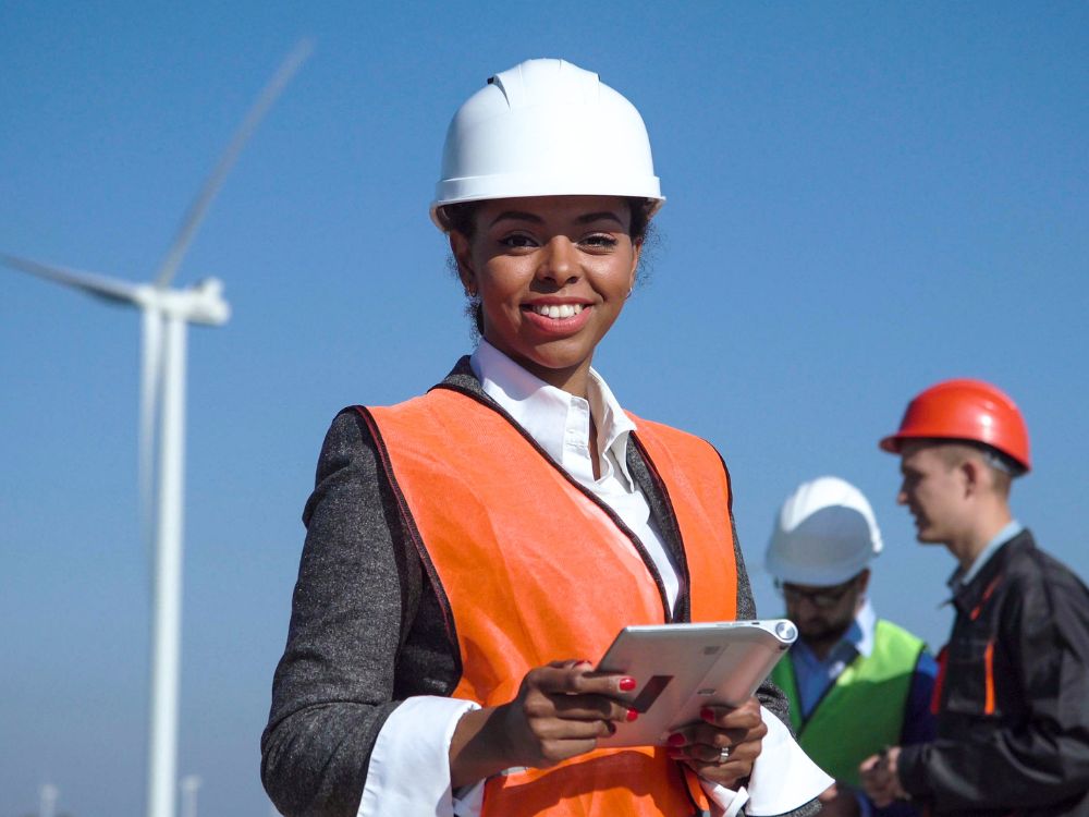 A Woman Holding A Tablet In Front Of Wind Turbines