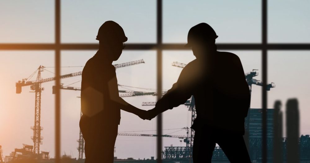 Two Construction Workers Shaking Hands In Front Of A Large Window With Construction Cranes In The Background Aspect Ratio 760 400
